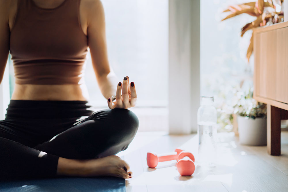 Woman sitting on floor meditating. Next to her there is two pink dumbbells.